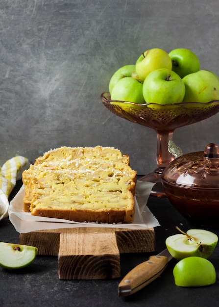 Maçã fatiada e bolo de coco na tábua de madeira em fundo escuro