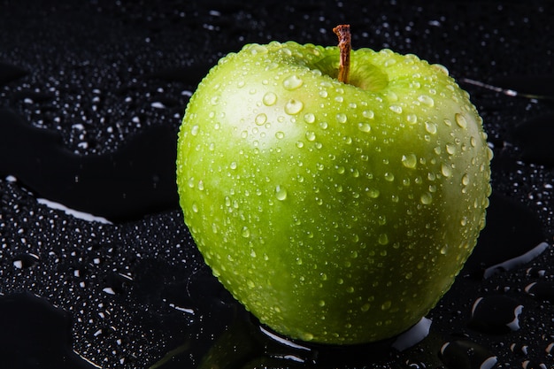 Maçã verde com gotas de chuva, sobre o vidro preto molhado