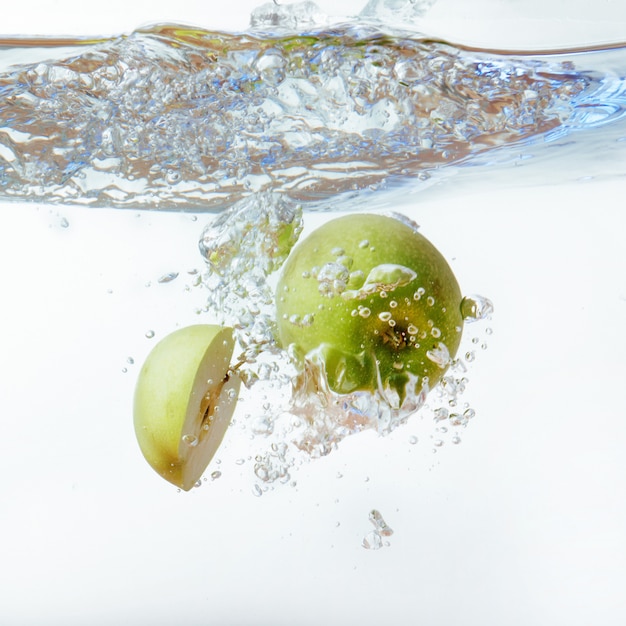 Maçã verde debaixo d'água com uma trilha de bolhas transparentes