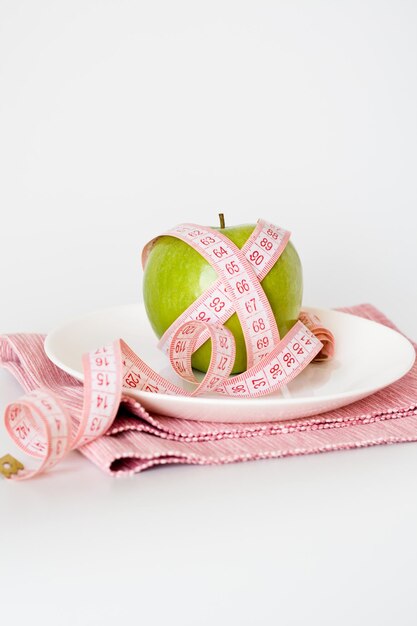 Maçã verde embrulhada em uma fita métrica em um prato branco e um guardanapo rosa em um fundo branco