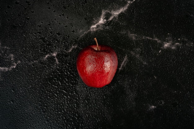 Foto maçã vermelha fresca com gotas de água encontra-se em um mármore preto, cheio de gotas de spray de água. vista superior plana leiga composição.