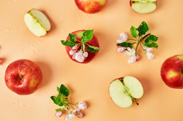 Maçã vermelha inteira fatiada e flores planas sobre um fundo laranja pastel