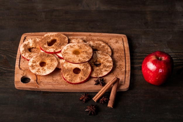 Maçã vermelha madura, dois bastões de canela, anis estrelado e tábua de cortar de madeira com fatias de frutas frescas polvilhadas com especiarias moídas