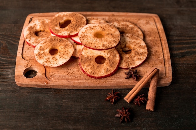 Maçã vermelha madura, dois bastões de canela, anis estrelado e tábua de cortar de madeira com fatias de frutas frescas polvilhadas com especiarias moídas