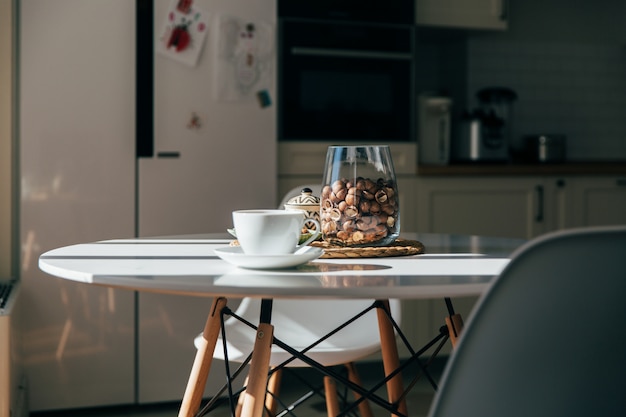 Macadamianüsse in einer Schüssel und eine Tasse Tee oder Kaffee stehen im Küchentisch, hartes Morgenlicht
