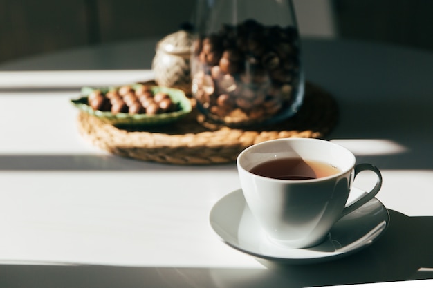 Macadamianüsse in einer Schüssel und eine Tasse Tee oder Kaffee stehen im Küchentisch, hartes Morgenlicht