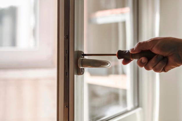 Maçaneta da janela de instalação Trabalhador manual instalando a fechadura na frente da porta de plástico com uma chave de fenda