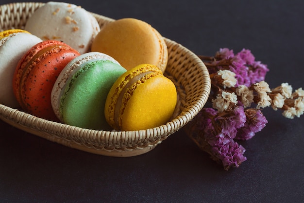 Macaron francés colorido o pila de macaron italiano en la cesta en la mesa de granito negro.