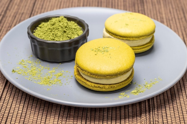 Macaron-Kuchen und Matcha-Teepulver auf einem grauen Teller und auf einer Serviette aus Holzstäbchen von oben