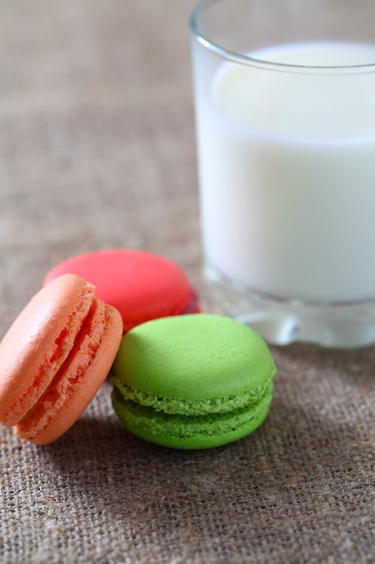 Macaron três peças vermelho, verde, laranja e vidro com leite na toalha de mesa de estopa.