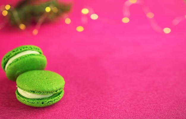 Macaron verde com fondant em fundo de papel vermelho. Perto de um galho de uma árvore de Natal com uma guirlanda. Close-up, copyspace.