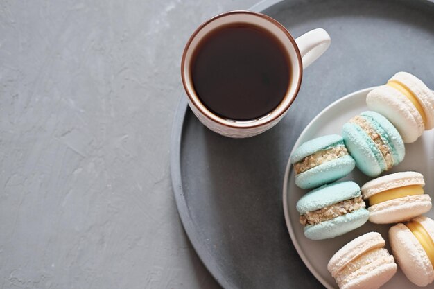 Foto macarones franceses y una taza de café sobre un fondo gris. macarones hechos en casa. buen día.