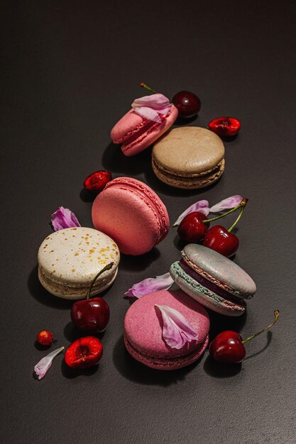 Macarones con pétalos de flores de peonías y cerezas maduras sobre un fondo de piedra negra Postre dulce