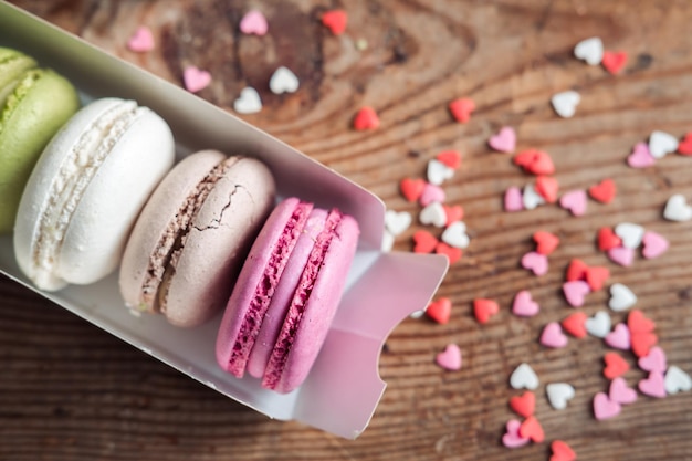 Macarones variados en una caja salpicada de pequeños corazones en una vista superior de fondo de madera