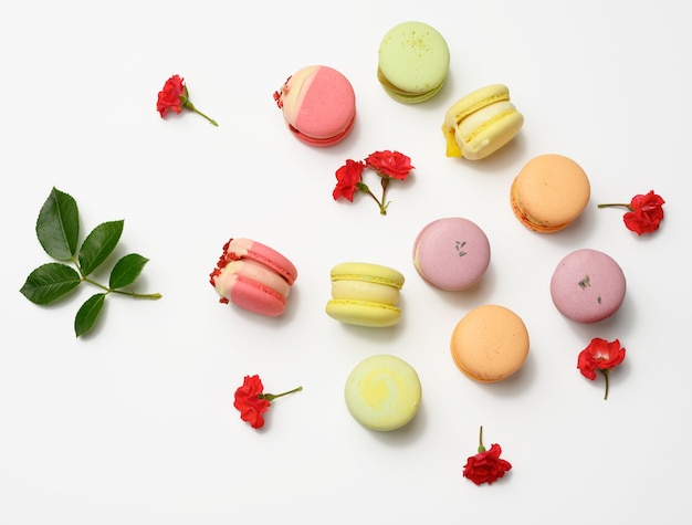 Macarons assados com diferentes sabores e botões de rosa em um fundo branco, vista de cima