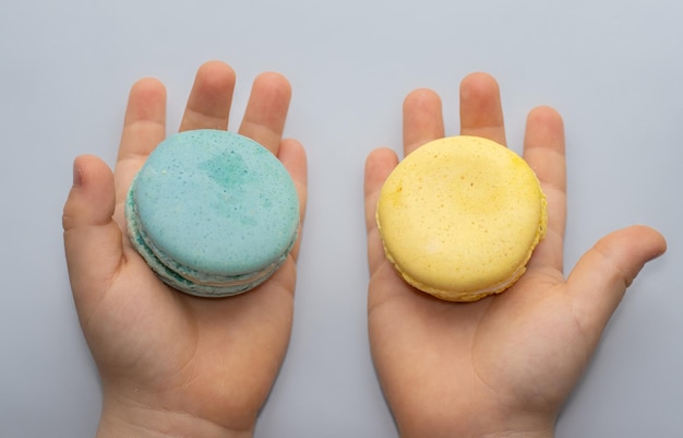 macarons azules y amarillos en la mano de un niño o en una superficie gris delicioso color del desierto