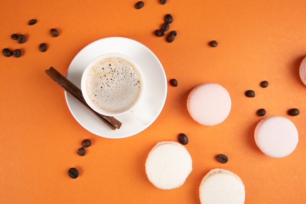 Macarons blancos y café con canela sobre una superficie naranja. semillas de cafe