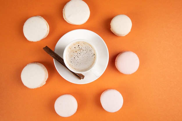 Macarons blancos y café con canela sobre una superficie naranja