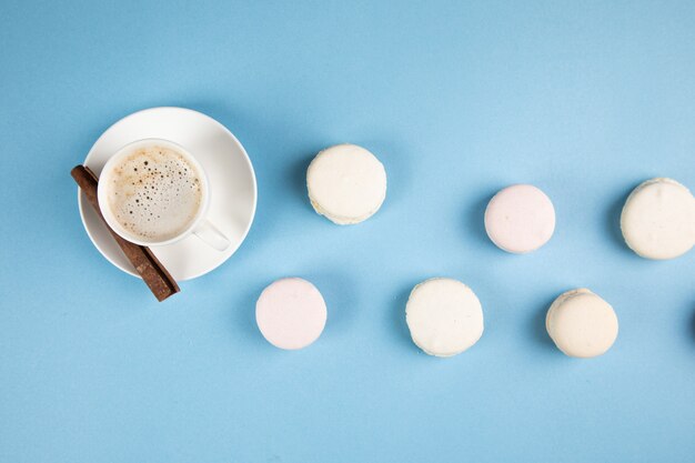 Macarons brancos e café com canela em uma superfície azul