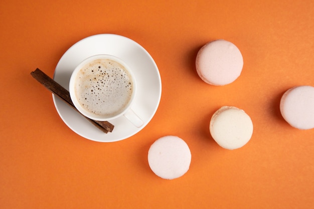 Macarons brancos e café com canela em uma superfície laranja