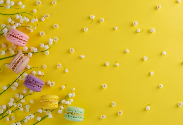 Macarons coloridos o macarrones decorados con flores florecientes de lirio de los valles en amarillo. Dulce concepto de postre francés. Composición de cuadros. Lay Flat. copyspace