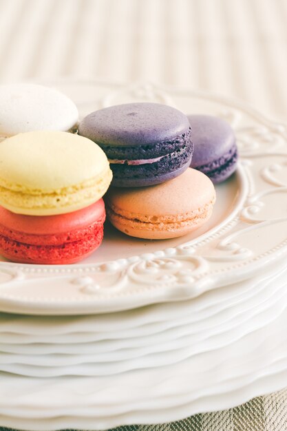 Macarons de diferentes colores en la pila de la placa en el pedestal de la torta blanca