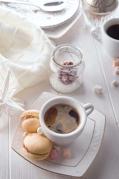 Macarons doces saborosos e xícara de café sobre fundo branco de madeira