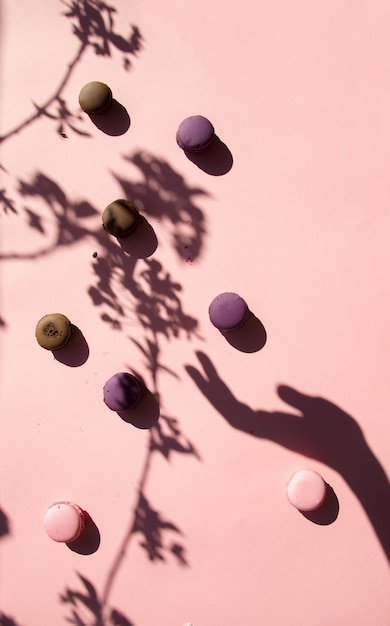 Macarons e sombra de mão feminina na superfície rosa