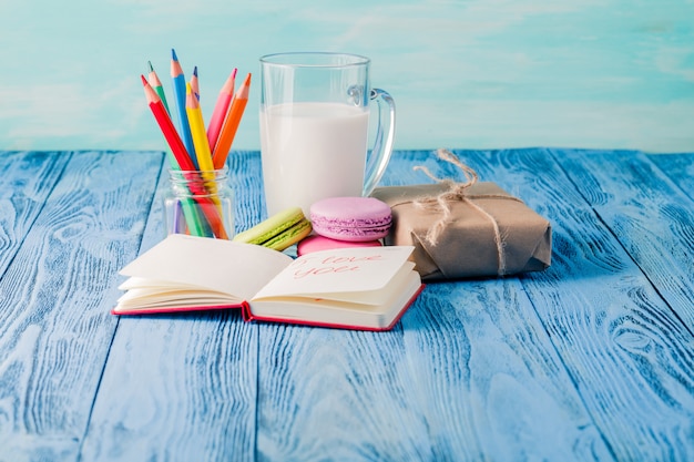 Macarons, ein Glas Milch. Buch- und Farbstifte