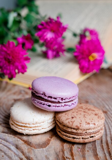 Macarons fondo rojo flores y libros, sobre una mesa de madera. Marco vertical. Estética con macarrones y flores. Hermosas tortas en una mesa de madera. Desayuno francés por la mañana.