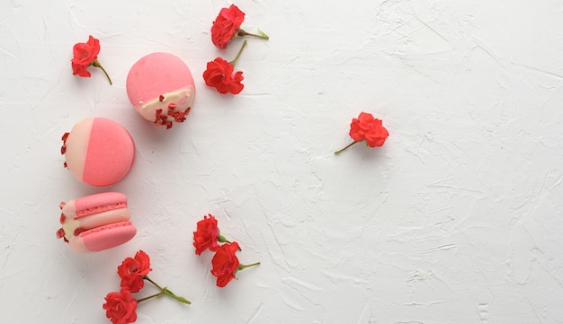 Macarons de fresa roja al horno y capullos de rosa sobre una mesa blanca, postre de harina de almendras gourmet, cerrar