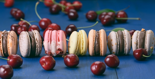 Macarons multicolores y cerezas rojas maduras sobre fondo de madera azul, cerrar