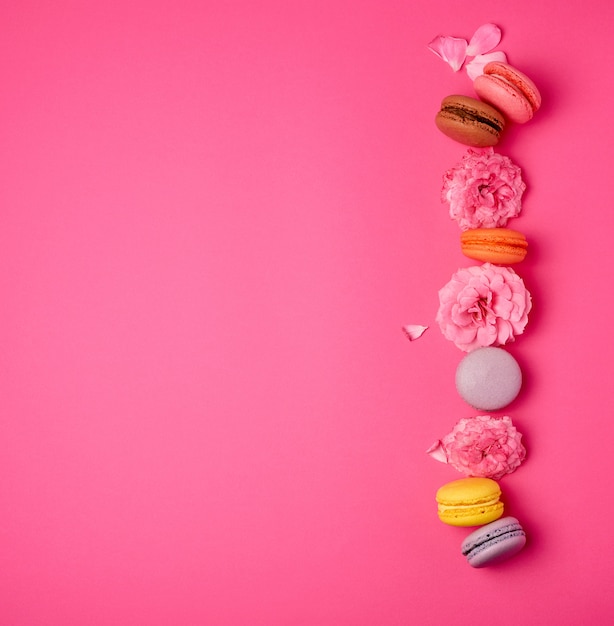 Macarons multicoloridos doces com creme e um botão de rosa cor de rosa