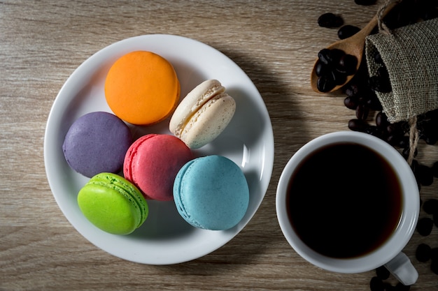 Macarons no prato branco com café preto em uma xícara e grãos de café no fundo da mesa de madeira
