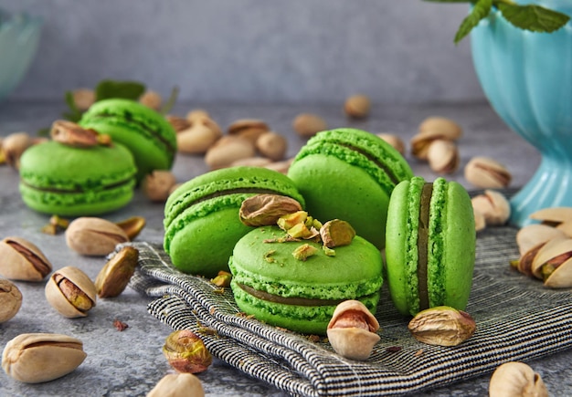 Macarons de pistacho de color verde con pistachos y menta sobre fondo de madera gris