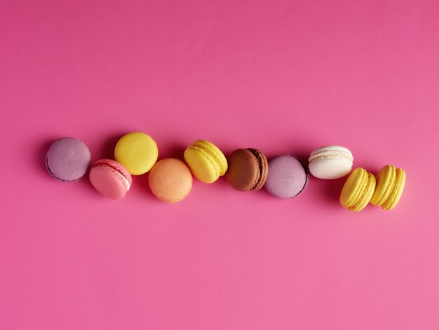 Los macarons redondos multicolores al horno con crema se encuentran en una línea en rosa