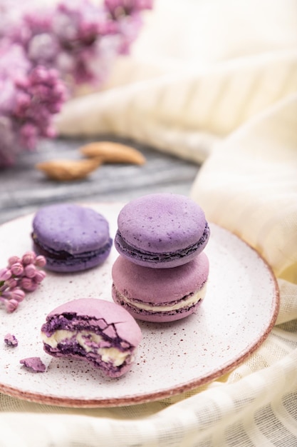 Macarons roxos ou bolos de macaroons com xícara de café em um fundo cinza de madeira e têxteis de linho branco. Vista lateral, close-up, foco seletivo.