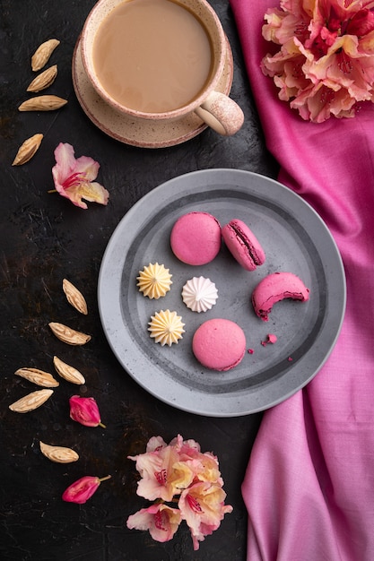 Macarons roxos ou bolos de macaroons com xícara de café em um fundo preto de concreto e têxteis rosa. Vista superior, configuração plana,