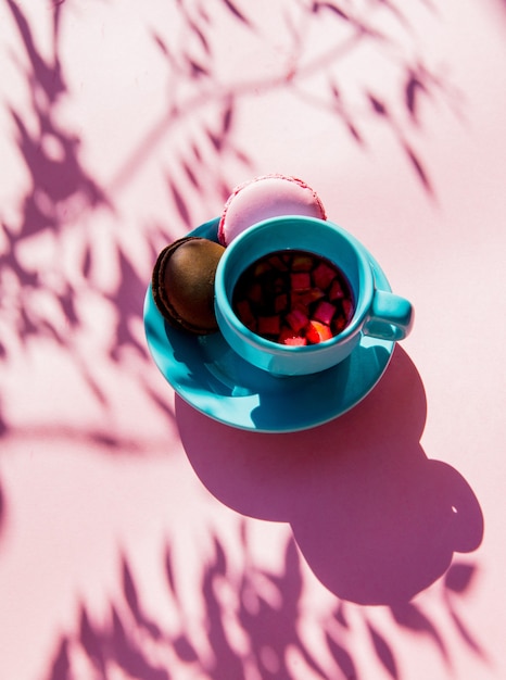 Macarons y taza de té con sombras sobre superficie rosa