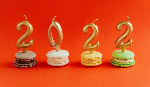 Macarons con velas encendidas 2022 sobre fondo rojo. Año nuevo.