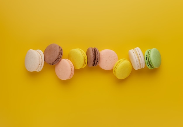 Foto macaroon. macaron de bolo colorido com tons pastel espalhados sobre fundo amarelo. vista superior de biscoitos de amêndoa.