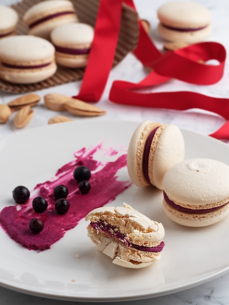 Macaroons caseiros em um prato cinza. Bagas de groselha e recheio de biscoitos em um prato. Fechar-se. laço vermelho