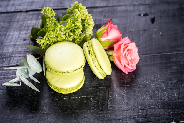 Macaroons coloridos doces em composição com flores em fundo preto. Copiar espaço