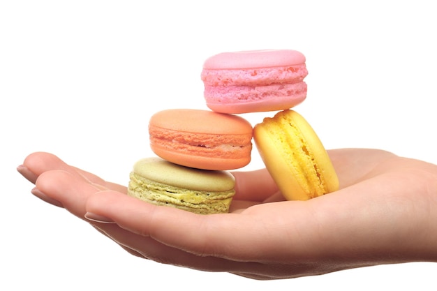 Macaroons coloridos saborosos na mão feminina isolados em branco