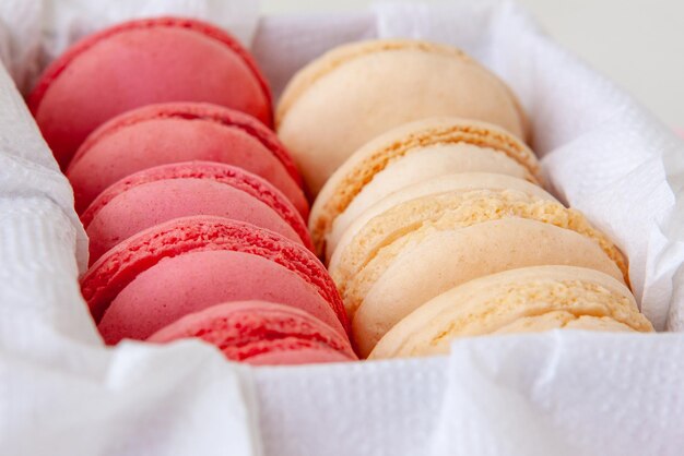 Macaroons de baunilha e morango em uma caixa em um guardanapo branco e doces