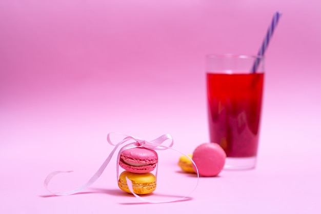 Foto macaroons de rosa e amarelos lindos são amarrados com fita e copo de bebida de frutas no fundo
