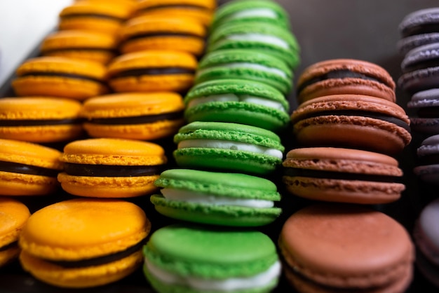 Macaroons em um fundo preto muita massa colorida com biscoitos franceses Macarons franceses marrons bege em um carrinho Presente para o dia dos namorados