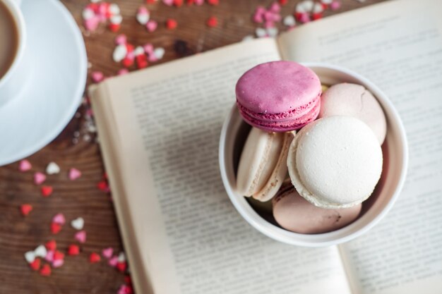 Macaroons em uma tigela uma xícara de café em um fundo de pequenos corações em um fundo de madeira