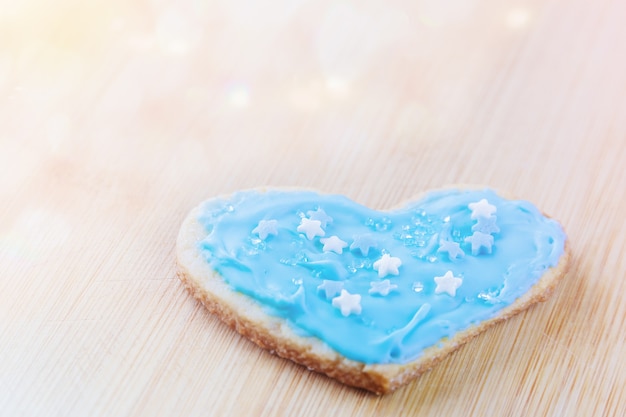 Macaroons festivos em forma de coração cobertos com glacê azul e polvilhados com estrelas de açúcar e cristais em uma placa de madeira