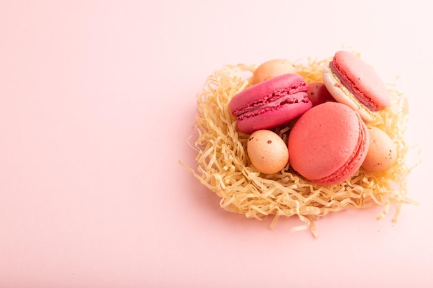 Macaroons magenta e rosa e ovos de chocolate em ninho de papel decorativo no espaço de cópia de vista lateral de fundo pastel rosa
